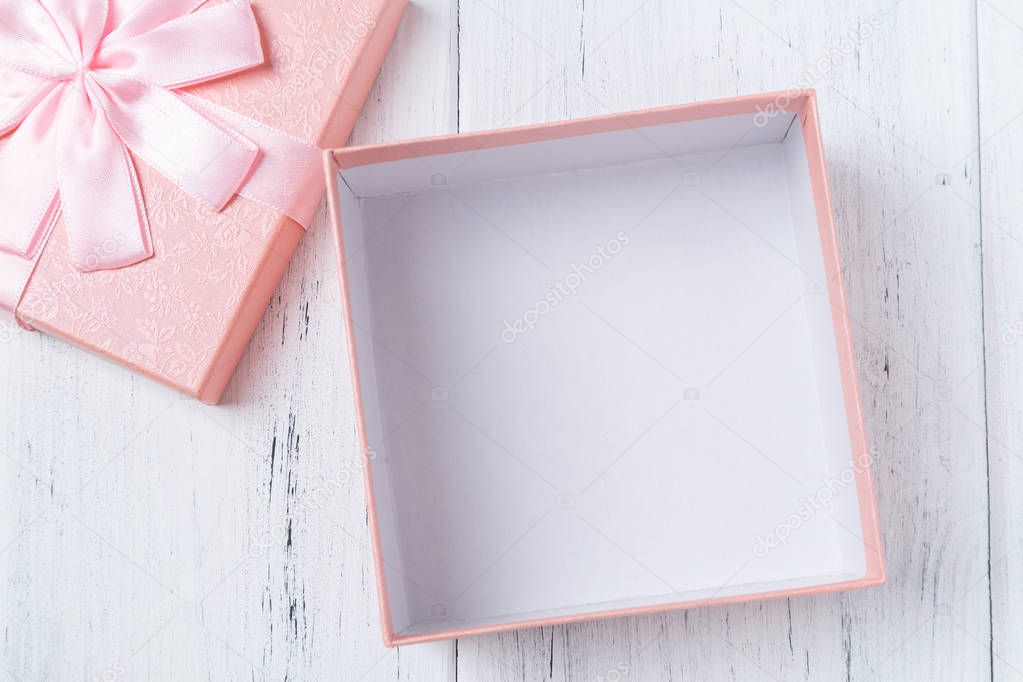 Opened empty decorative pink gift box with bow on wooden table. Mockup