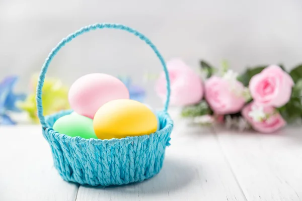 Fondo de Pascua. Cesta de huevos de colores sobre mesa de madera con flores de primavera — Foto de Stock