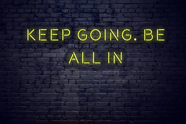 Positive inspiring quote on neon sign against brick wall keep going be all in