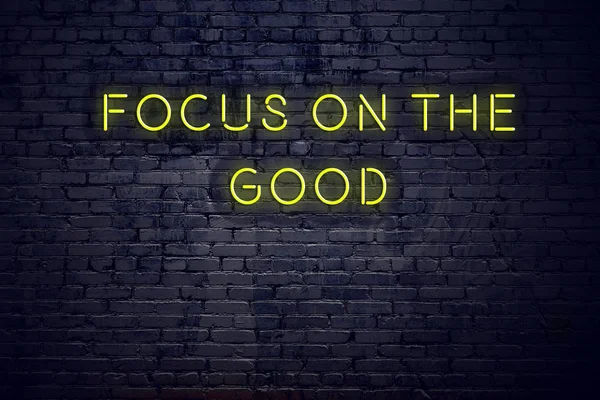 Positive inspiring quote on neon sign against brick wall focus on the good