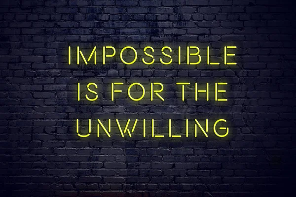 Positive inspiring quote on neon sign against brick wall impossible is for the unwilling