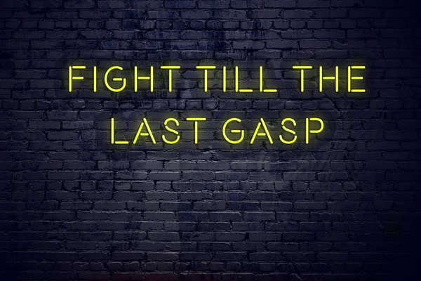 Positive inspiring quote on neon sign against brick wall fight till the last gasp