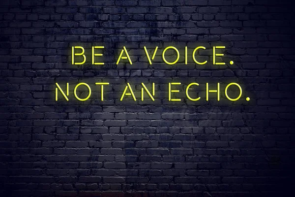 Positive inspiring quote on neon sign against brick wall be a voice not an echo