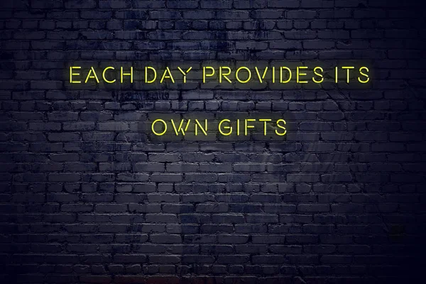Positive inspiring quote on neon sign against brick wall each day provides its own gifts