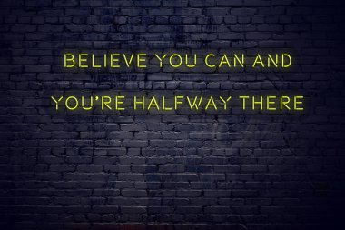 Positive inspiring quote on neon sign against brick wall believe you can and youre halfway there clipart
