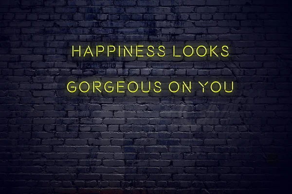 Positive inspiring quote on neon sign against brick wall happiness looks gorgeous on you