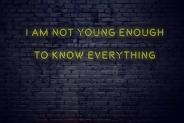 Positive inspiring quote on neon sign against brick wall i am not young enough to know everything