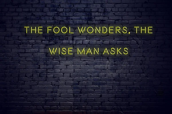 Positive inspiring quote on neon sign against brick wall the fool wonders the wise man asks — Stockfoto