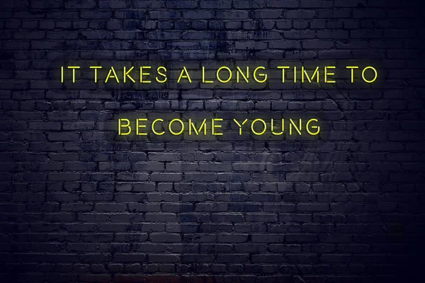 Positive inspiring quote on neon sign against brick wall it takes a long time to become young