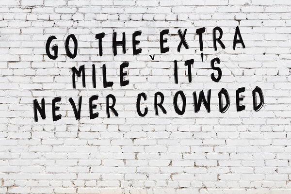 Стена из белого кирпича с раскрашенной черной мотивационной надписью
