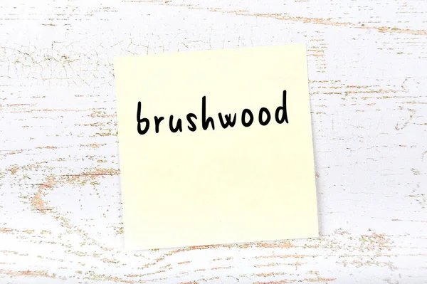 Folha de papel amarelo com brushwood palavra. Conceito de lembrete — Fotografia de Stock