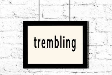 Beyaz tuğla duvarda asılı siyah çerçeve ve titreyen yazılar.