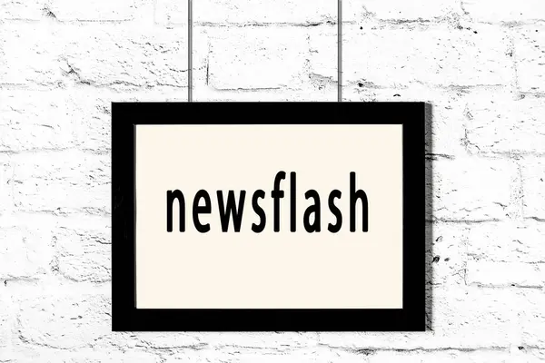 Montatura nera appesa al muro di mattoni bianchi con iscrizione newsflash — Foto Stock