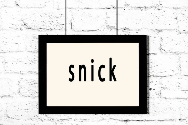 Black frame hanging on white brick wall with inscription snick — Stock Photo, Image