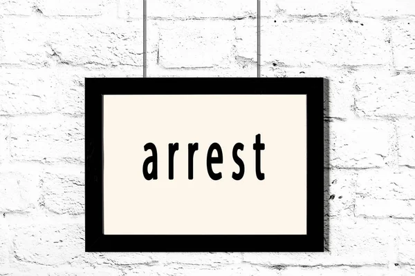 Black frame hanging on white brick wall with inscription arrest — Stock Photo, Image