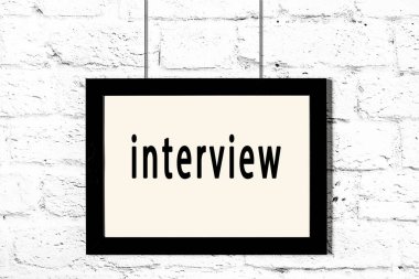 Beyaz tuğla duvarda asılı siyah çerçeve ve yazı röportajı