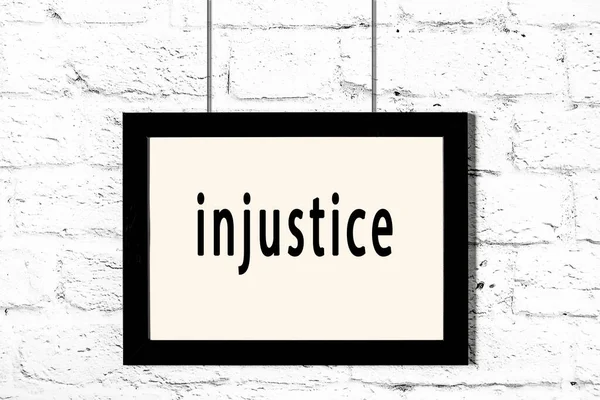 Black frame hanging on white brick wall with inscription injustice — Stock Photo, Image