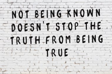 Beyaz tuğla duvara zekice alıntılar yazılı siyah bir yazı.