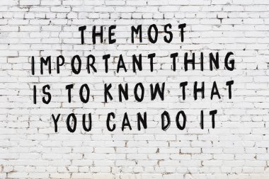 Beyaz tuğla duvara zekice alıntılar yazılı siyah bir yazı.