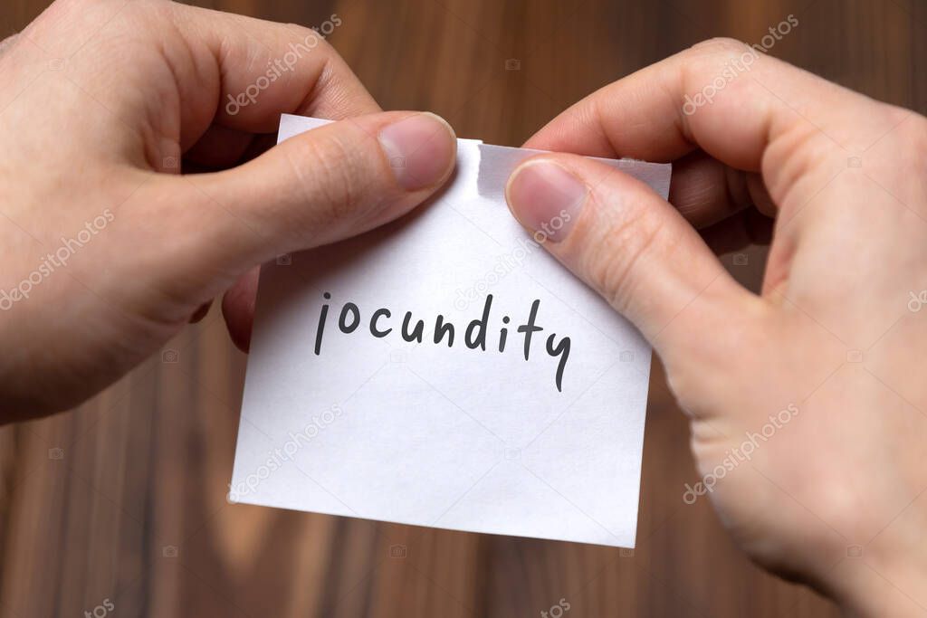 Hands of a man tearing a piece of paper with inscription jocundity