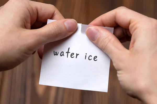 Handen van een man die een stuk papier scheurt met de inscriptie water ijs — Stockfoto