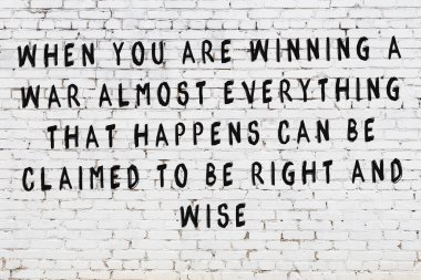 Beyaz tuğla duvara zekice alıntılar yazılı siyah bir yazı.