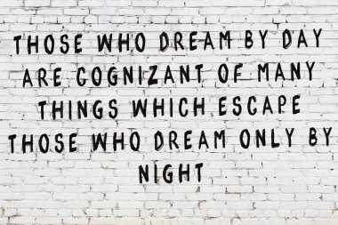 Beyaz tuğla duvara zekice alıntılar yazılı siyah bir yazı.