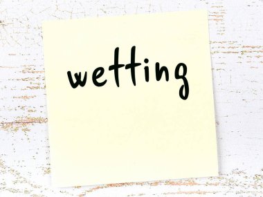 Tahta duvarda sarı yapışkan bir not ve el yazısı ile ıslatılıyor.