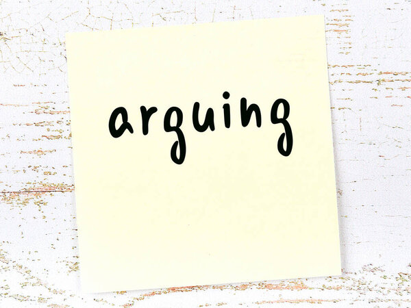 Yellow sheet of paper with word arguing. Reminder concept