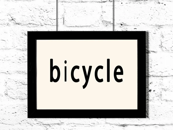 Black frame hanging on white brick wall with inscription bicycle — Stock Photo, Image