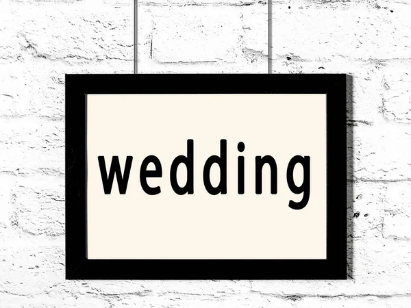 Černý rám zavěšený na zdi z bílých cihel s nápisem svatba — Stock fotografie