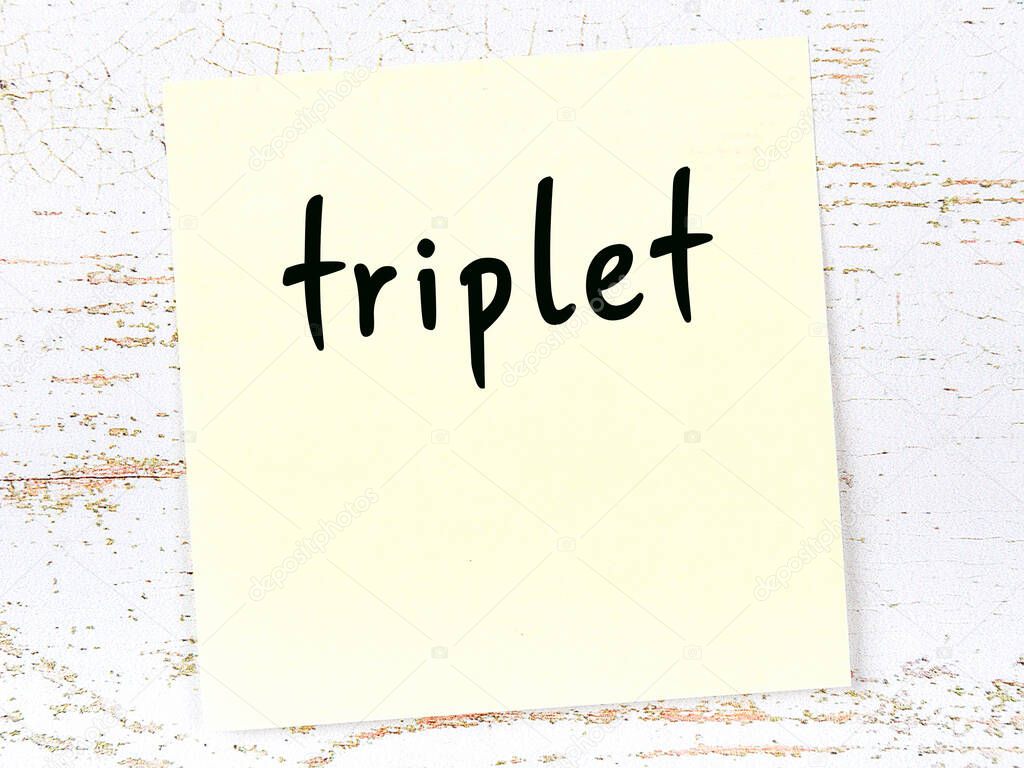 Yellow sticky note on wooden wall with handwritten word triplet