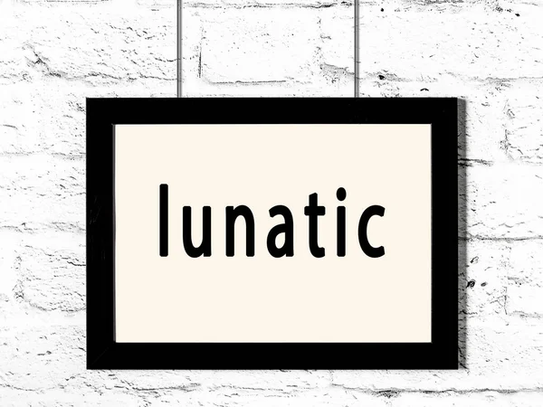 Black frame hanging on white brick wall with inscription lunatic — Stock Photo, Image