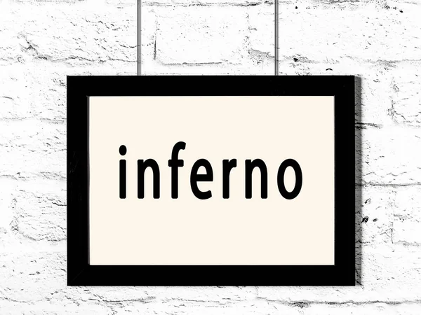 Cadre noir accroché au mur de briques blanches avec inscription inferno — Photo