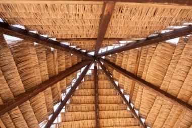 Kurumuş palmiye yaprakları ve ahşap kirişlerden yapılmış geleneksel sazdan çatının yakın görüntüsü geometrik desen oluşturuyor. Sık sık kulübelerde, çardaklarda bulunan tropikal bir yapı. Sejile Sahili.