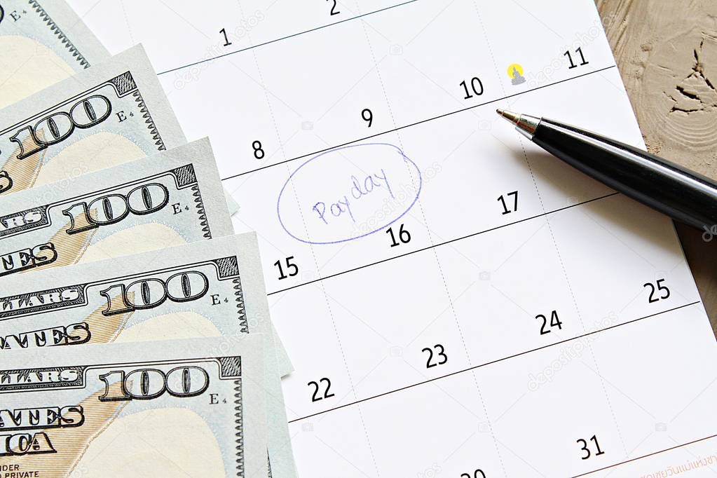 Business, finance, savings money, wages, payroll or accounting concept : Calendar with blue marker circle in word payday and American dollars cash money for remind
