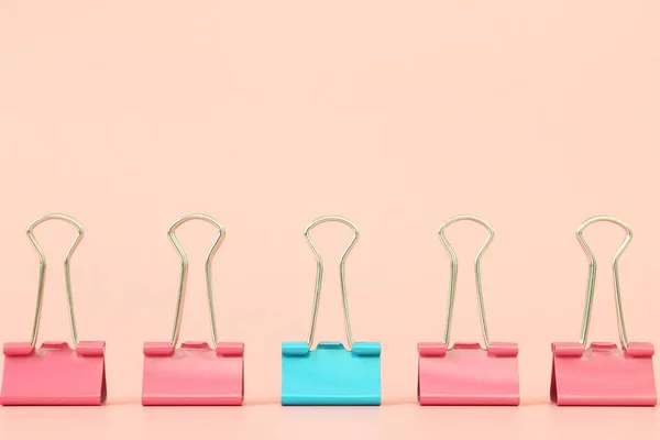 Business, office supplies, leadership, unique, individuality or think different concept : Blue binder clip standing out of pink binder clips on orange background with copy space for adding or mock up