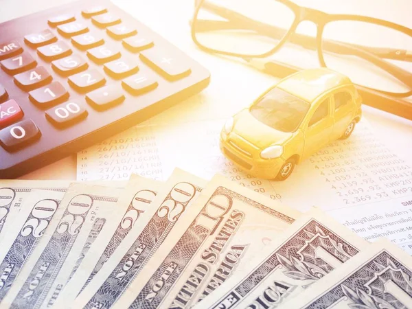Business, finance, saving money or car loan concept : Top view or flat lay of miniature car model, American Dollars cash money, calculator and saving account book or financial statement on office desk