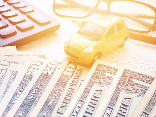 Business, finance, saving money or car loan concept : Miniature car model, American Dollars cash money, calculator and saving account book or financial statement on office desk table