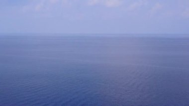 Mavi okyanus kıyısında beyaz kum arka planlı sakin bir sahil yolculuğunun insansız hava aracı manzarası