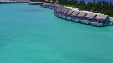 Lüks tatil köyü kumsal saatinde, turkuaz deniz kenarında beyaz kumlu arka planda hava aracı gökyüzü.