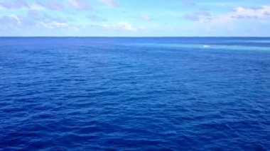 Beyaz kumlu arka planlı mavi okyanus kıyısındaki sakin sahil saatinin insansız hava aracı soyutlaması.