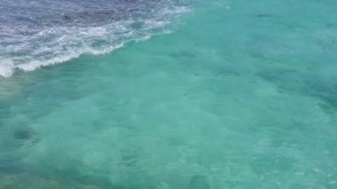 Rahatlatıcı sahil manzarası beyaz kum arka planıyla berrak okyanus tarafından kırılıyor.