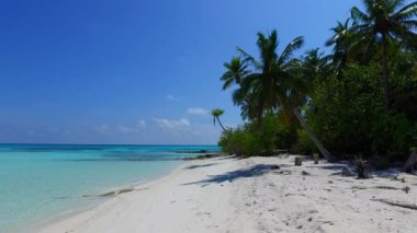Lüks turist plajlarının güneşli deniz manzarası gün batımından önce beyaz kum arka planıyla mavi deniz kıyısında kırılıyor.