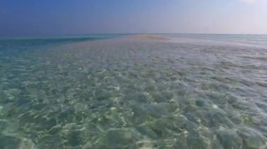 Mavi deniz kıyısındaki lüks sahil seyahatinin güneşli manzarası ve kumsalın yanındaki kumlu arka plan.