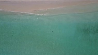Sahil kenarındaki temiz kumlu arka planda su mavisi deniz kıyısındaki sakin tatil beldesinin güneşli doğası.