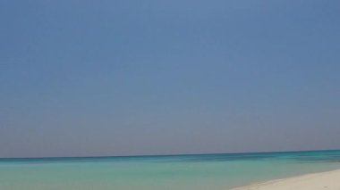 Huzurlu sahil sahili tatil manzarası. Su mavisi suların yanında, tatil köyünün yakınında beyaz kumlu bir arka plan.