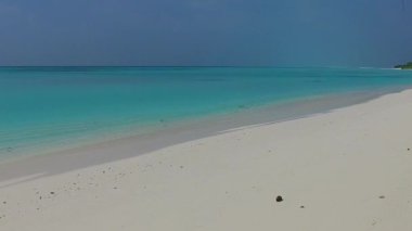 Lüks sahil plajlarının güneşli deniz manzarası şeffaf su ve tatil köyü yakınlarındaki beyaz kumlu arka planla kesiliyor.