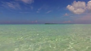 Mavi deniz kıyısındaki güneşli deniz manzarası ve kumsal kenarındaki temiz kum zemini.