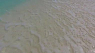 Güneşli, sakin bir tatil köyü sahili. Mavi okyanus kıyısında, beyaz kumlu arka plan güneş ışığı altında.